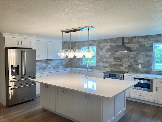 kitchen with premium appliances, a kitchen island with sink, wall chimney exhaust hood, white cabinetry, and dark hardwood / wood-style flooring