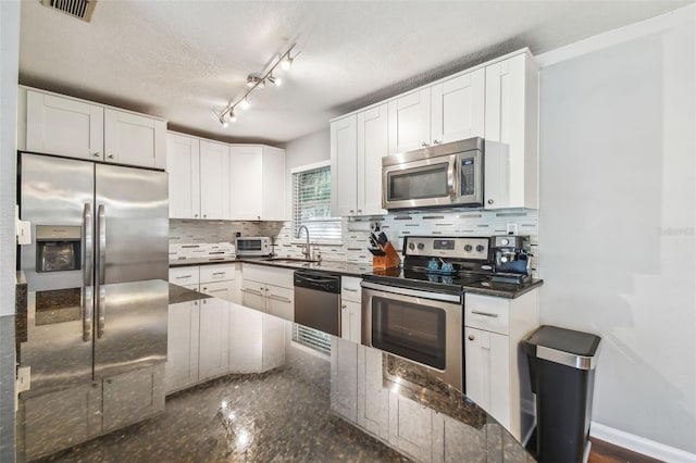 kitchen with backsplash, a textured ceiling, stainless steel appliances, white cabinets, and dark stone countertops