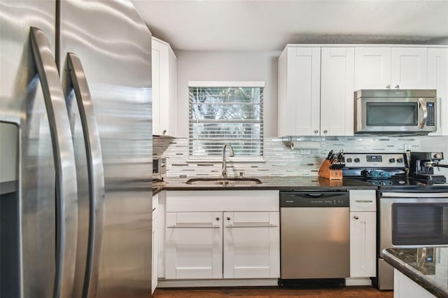 kitchen with tasteful backsplash, appliances with stainless steel finishes, sink, white cabinets, and dark stone countertops