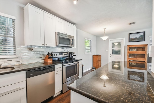 kitchen with appliances with stainless steel finishes, white cabinetry, dark stone counters, dark wood-type flooring, and decorative light fixtures