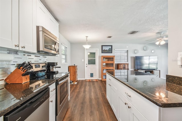 kitchen with hanging light fixtures, stainless steel appliances, white cabinets, decorative backsplash, and dark hardwood / wood-style floors