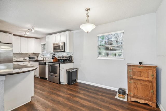 kitchen with backsplash, white cabinets, decorative light fixtures, appliances with stainless steel finishes, and dark hardwood / wood-style flooring