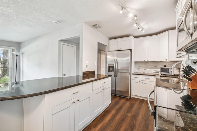 kitchen featuring dark wood-type flooring, stainless steel appliances, dark stone countertops, white cabinetry, and a textured ceiling