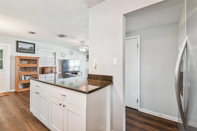 kitchen with dark hardwood / wood-style flooring, stainless steel fridge, white cabinetry, ceiling fan, and dark stone countertops