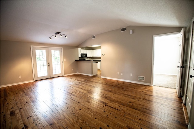 unfurnished living room featuring vaulted ceiling, a textured ceiling, french doors, and dark wood-type flooring