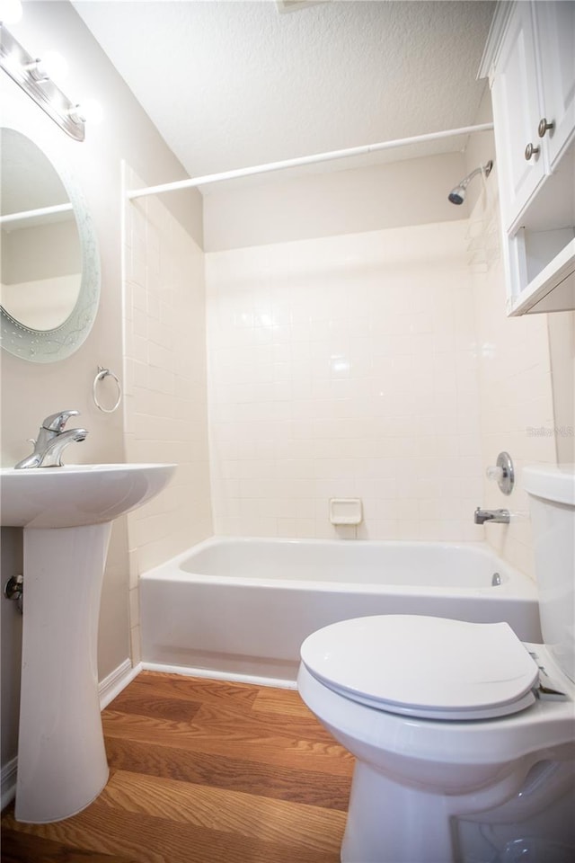 bathroom with a textured ceiling, toilet, tiled shower / bath combo, and hardwood / wood-style flooring