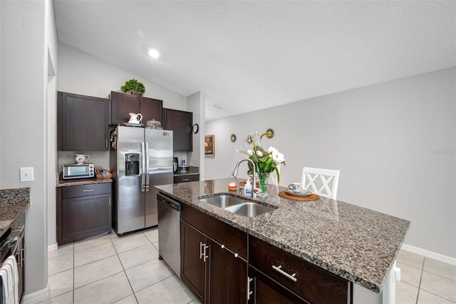 kitchen with a kitchen island with sink, sink, light stone countertops, appliances with stainless steel finishes, and lofted ceiling