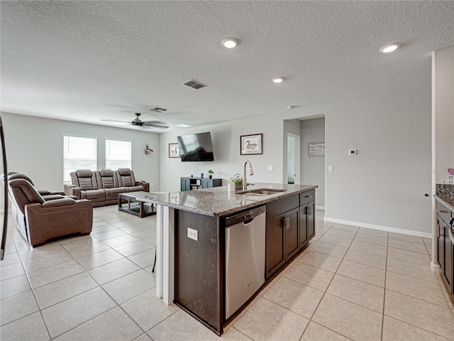 kitchen with light stone counters, sink, an island with sink, ceiling fan, and stainless steel dishwasher