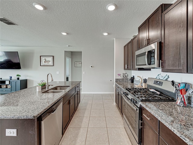 kitchen featuring an island with sink, stainless steel appliances, sink, and light stone counters