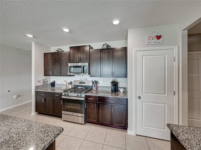 kitchen with appliances with stainless steel finishes, dark brown cabinets, light tile patterned floors, and light stone countertops