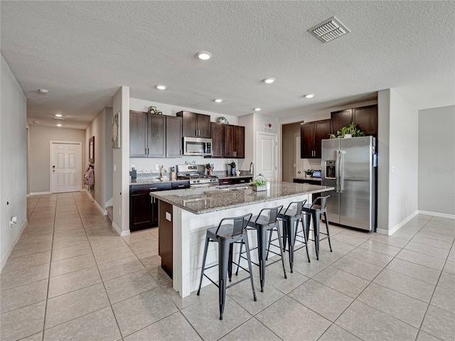 kitchen with light stone counters, an island with sink, sink, a breakfast bar, and appliances with stainless steel finishes