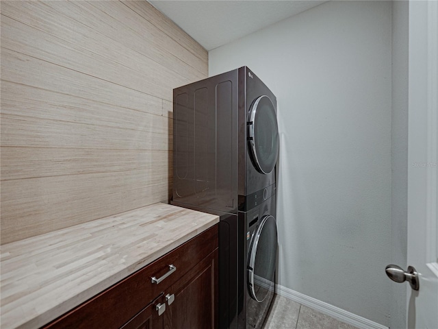 laundry area featuring cabinets, stacked washer / dryer, and light tile patterned flooring