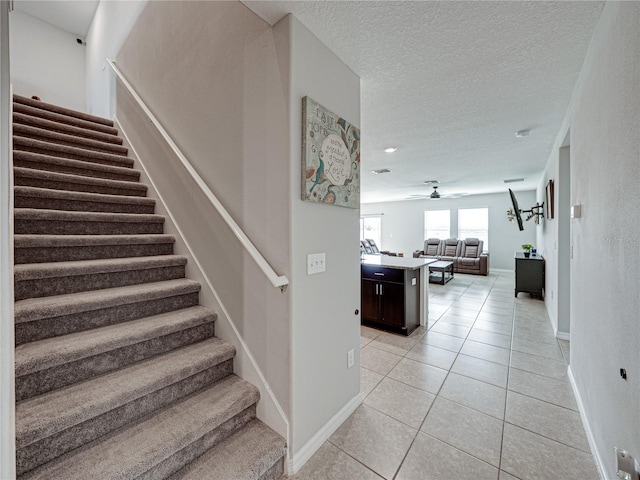 stairs featuring tile patterned flooring, ceiling fan, and a textured ceiling