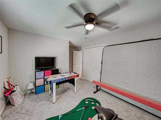 rec room with a textured ceiling, ceiling fan, and light carpet