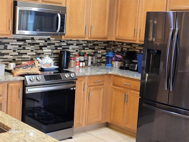 kitchen featuring stainless steel appliances, light stone countertops, backsplash, and light tile patterned flooring