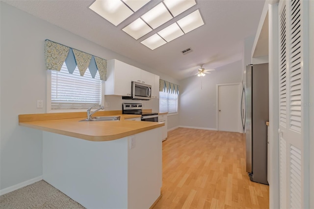 kitchen with light wood-type flooring, stainless steel appliances, sink, kitchen peninsula, and ceiling fan