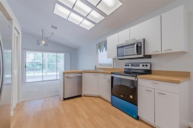 kitchen with a wealth of natural light, stainless steel appliances, white cabinetry, and light hardwood / wood-style flooring