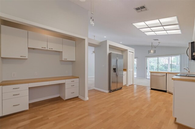 kitchen featuring built in desk, vaulted ceiling, appliances with stainless steel finishes, light hardwood / wood-style floors, and white cabinetry