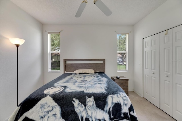 bedroom with light colored carpet, a textured ceiling, ceiling fan, and a closet