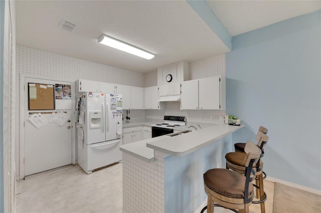 kitchen featuring white appliances, a kitchen bar, kitchen peninsula, decorative backsplash, and white cabinets