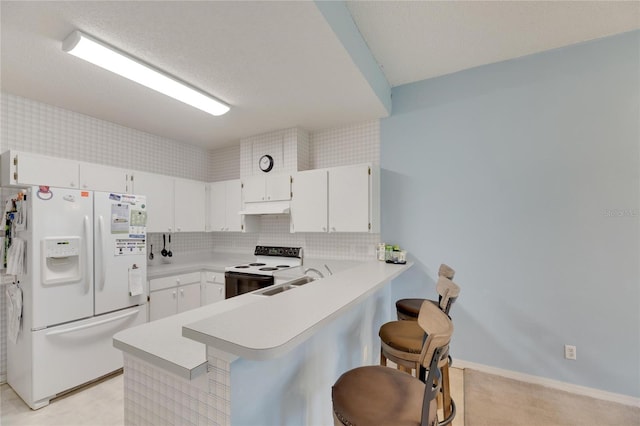 kitchen featuring a kitchen bar, kitchen peninsula, white appliances, and tasteful backsplash