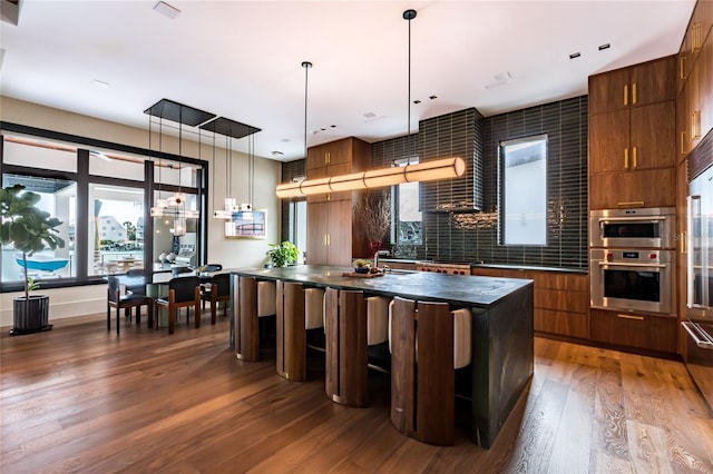 kitchen with decorative light fixtures, a kitchen bar, a center island, dark wood-type flooring, and stainless steel double oven