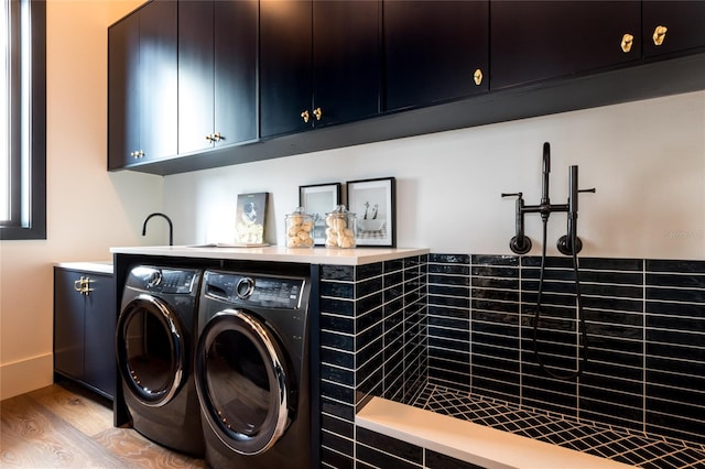 clothes washing area with light wood-type flooring, cabinets, washing machine and clothes dryer, and bar