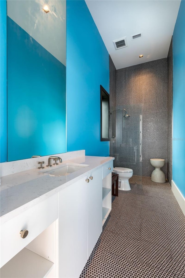 bathroom featuring vanity, toilet, tiled shower, and tile patterned floors