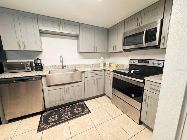 kitchen with gray cabinetry, stainless steel appliances, light tile patterned flooring, and sink