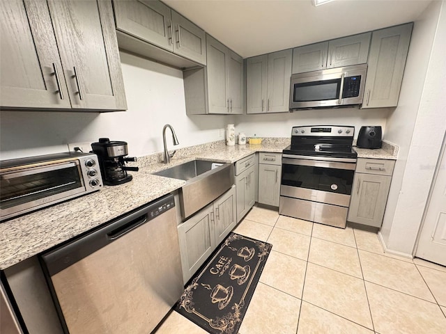 kitchen with appliances with stainless steel finishes, light tile patterned flooring, sink, and light stone countertops