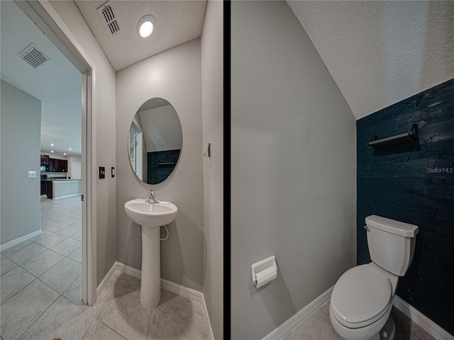 bathroom with toilet, vaulted ceiling, tile patterned floors, and a textured ceiling