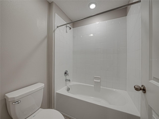 bathroom featuring toilet, a textured ceiling, and tiled shower / bath