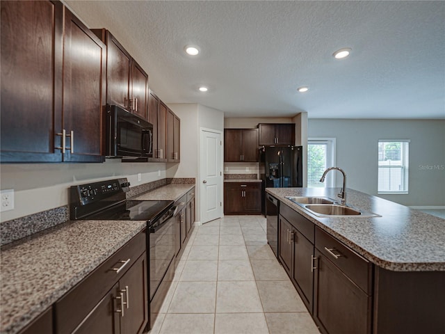 kitchen featuring black appliances, sink, dark brown cabinetry, a kitchen island with sink, and light tile patterned floors