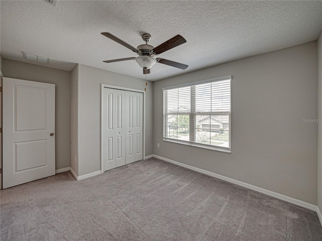 unfurnished bedroom featuring ceiling fan, a closet, light carpet, and a textured ceiling