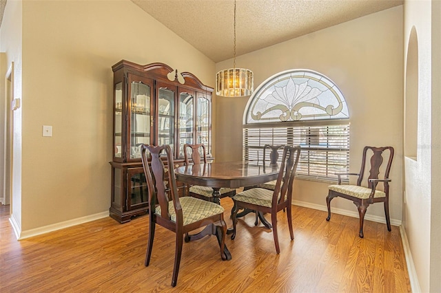 dining room with an inviting chandelier, vaulted ceiling, light hardwood / wood-style flooring, and a textured ceiling