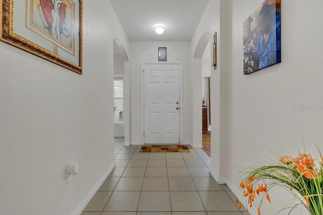 entryway featuring light tile patterned floors, baseboards, arched walkways, and a textured ceiling