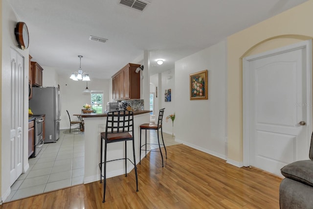 kitchen with hanging light fixtures, kitchen peninsula, stainless steel appliances, and light hardwood / wood-style floors