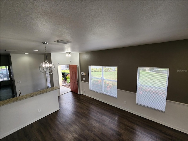 unfurnished living room with a textured ceiling, dark wood-type flooring, and a chandelier