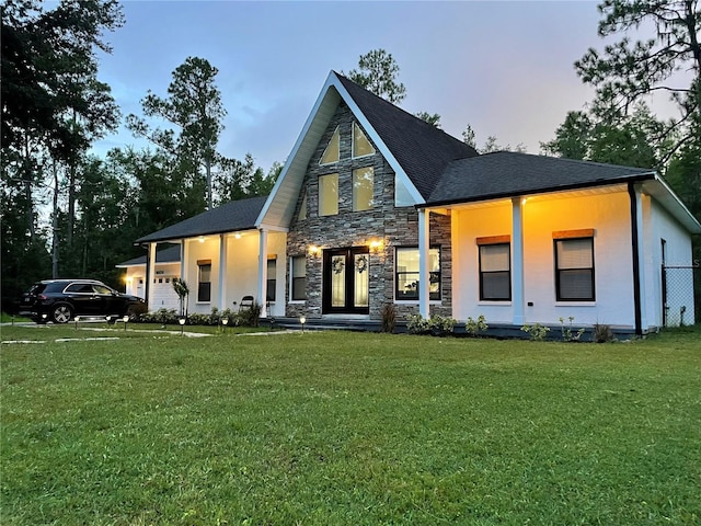 rear view of house featuring a garage, stone siding, and a lawn