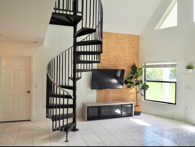 staircase featuring high vaulted ceiling, marble finish floor, a textured ceiling, and baseboards