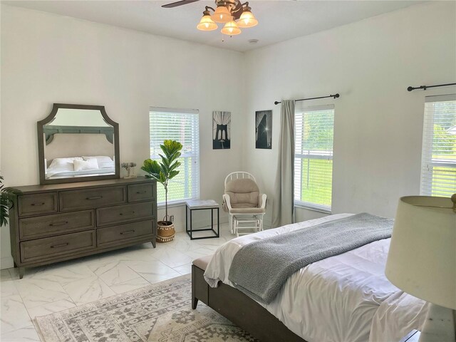 bedroom featuring a ceiling fan, marble finish floor, and multiple windows