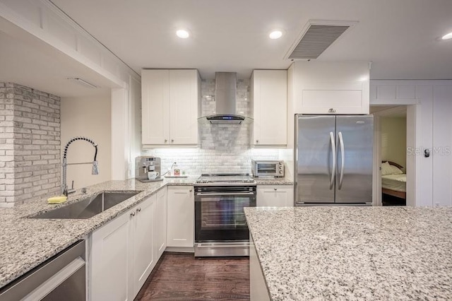 kitchen with wall chimney exhaust hood, appliances with stainless steel finishes, sink, and white cabinets