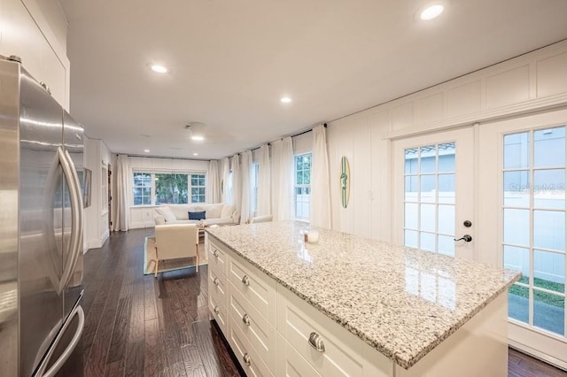 kitchen with a kitchen island, light stone countertops, stainless steel fridge, dark hardwood / wood-style flooring, and white cabinets