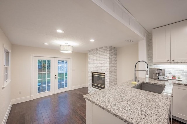 kitchen with a fireplace, dark wood-type flooring, sink, light stone counters, and white cabinets