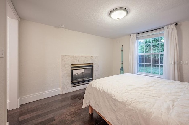 bedroom with a textured ceiling, dark wood-type flooring, and a multi sided fireplace