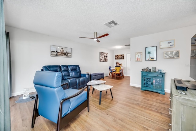 living room featuring ceiling fan, light wood-type flooring, and a textured ceiling