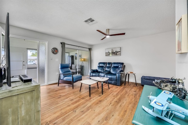 living room featuring ceiling fan, light wood-type flooring, and a textured ceiling