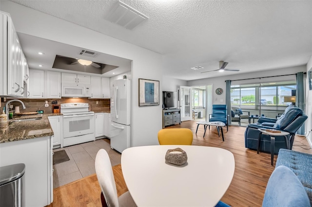 dining space with ceiling fan, a raised ceiling, sink, light wood-type flooring, and a textured ceiling