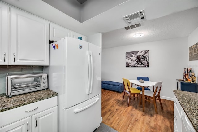 kitchen with white cabinets, decorative backsplash, dark stone counters, and white fridge