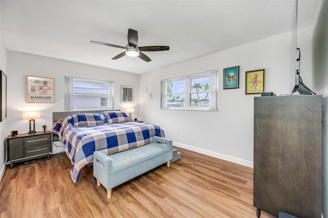 bedroom with ceiling fan, multiple windows, a textured ceiling, and light hardwood / wood-style floors